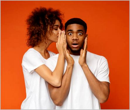 Hidden desires. Black woman whispering her dreams to shocked boyfriend, orange studio background